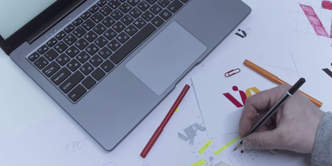 Creative workplace of a Graphic Designer. A man in the office is developing a logo on the table against the background of printed sketches and a laptop.