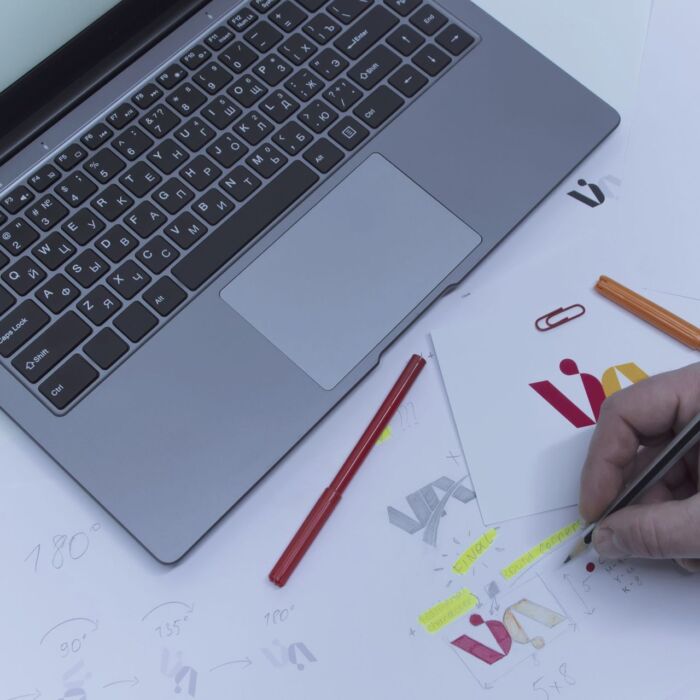 Creative workplace of a Graphic Designer. A man in the office is developing a logo on the table against the background of printed sketches and a laptop.