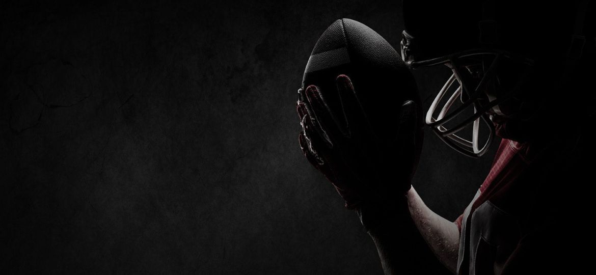 American football player standing with rugby helmet and ball against full frame shot of concrete wall